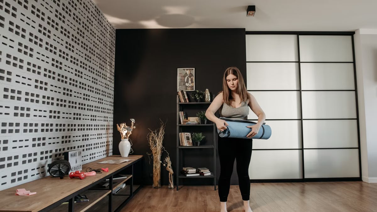 Plus size woman rolling a yoga mat in a stylish indoor setting with modern decor.