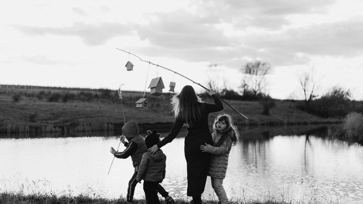 A mother and her children enjoy a serene moment at a lakeshore, captured in black and white.
